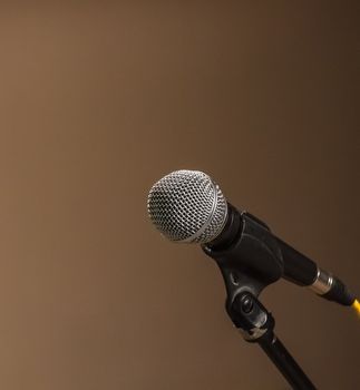 Classic black microphone on black stand. Isolated brown background