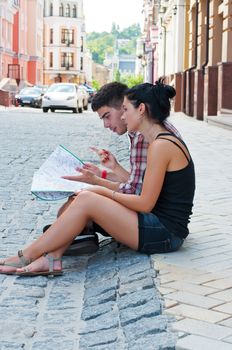 Girl and a guy sitting on street with map during the tourist walk.