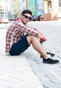 Young man sits on side of street.