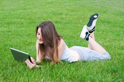 Happy smiling girl with tablet lying on grass.