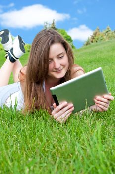 Smiling happy girl lying on grass in park with tablet.