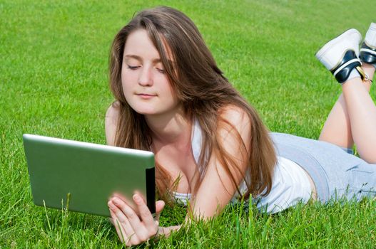 Girl student lying on grass with tablet.