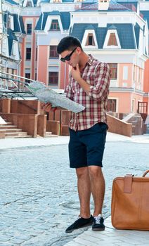 Young man with a suitcase in a thoughtful look at the map on city street.