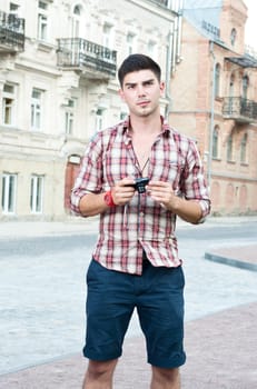 Young man with a compact camera stands on the street.