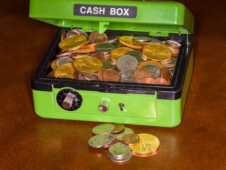 Green cash box with combination lock open to show piles of coins including gold and silver