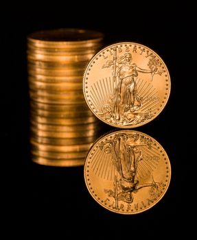 Reflection of single gold coin and stack on black polished surface