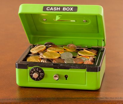 Green cash box with combination lock open to show piles of coins including gold and silver