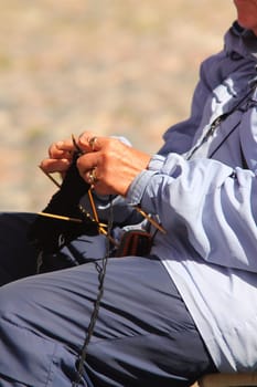 Elderly woman knitting a rug outdoors, sitting