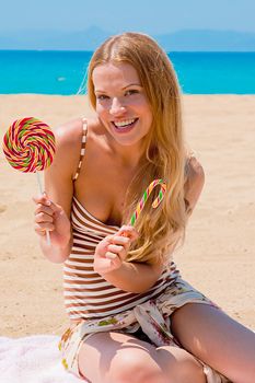 A young and beautiful woman with a lollipop resting on the beach