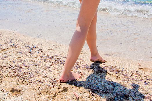 Photo of women's feet stepping along the sea beach in the background waves