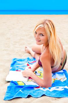 A young and beautiful woman resting on a beach reading a book in hard cover green