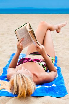 A young and beautiful woman resting on a beach reading a book in hard cover green