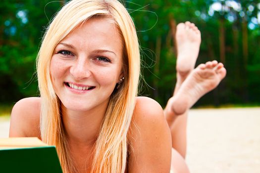 A young and beautiful woman resting on a beach reading a book in hard cover green