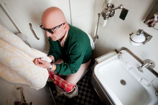 Adult male with sunglasses sitting on a toilet i train, wiping his hands with towel