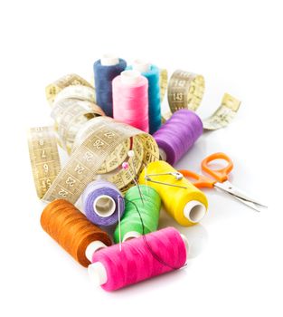 Sewing items: multicoloured threads, pins, meter and scissors on white