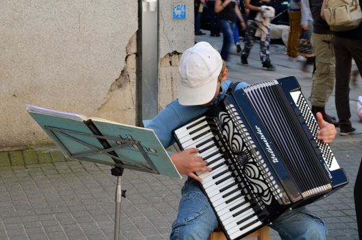 VILNIUS, LITHUANIA MAY 2012. Young child with cap plays ancient accordion. Street Musician Day.