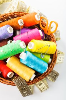 Sewing items in basket: threads, pins, meter and scissors on white