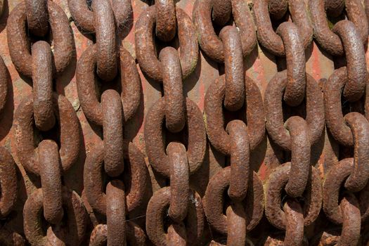 An old rusty chain with patterned vertical links on a red rust background.