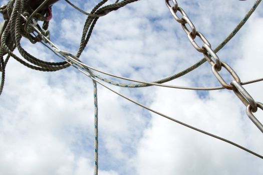 A white metal linked chain with rust lays over a cable and rope against a blue cloud sky.