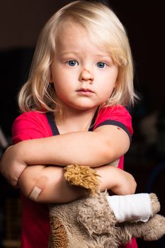 An injured cute little boy with band aid on his elbow, holding a toy puppy dog.