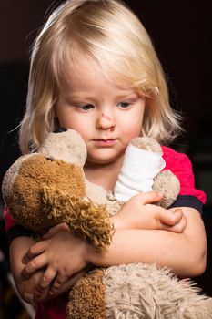 A cute injured little boy looking sad holding his stuffed dog toy.