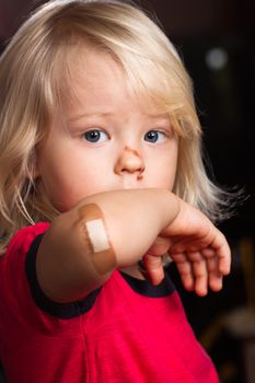A young injured boy showing his elbow with  band aid on.