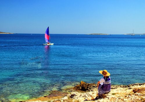 Young woman observing small sailing ship.