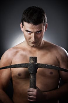 Topless construction worker with pick axe over grey background