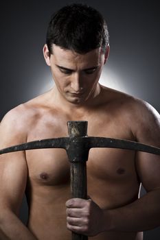 Topless construction worker with pick axe over grey background