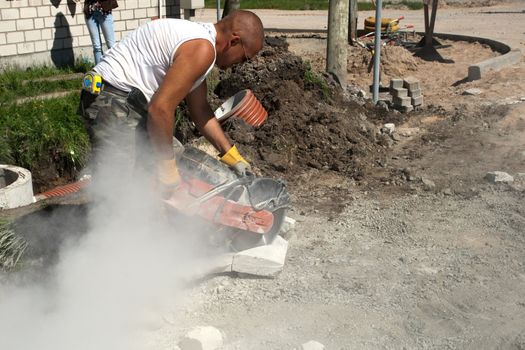 Road construction worker using a gas powered circular saw to cut concrete block