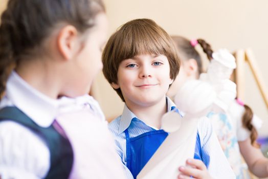 boy draws in the classroom with the other children, the children stand in a row in the table