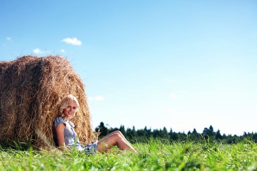 portrait of a girl next to a stack of hay under the blue sky