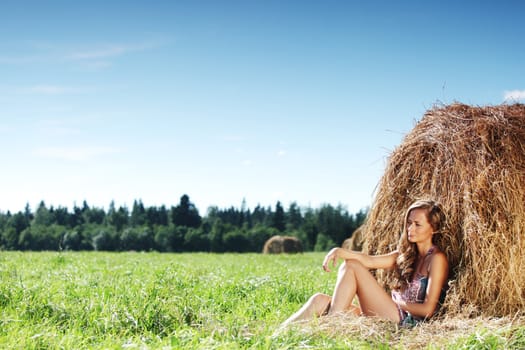 portrait of a girl next to a stack of hay under the blue sky