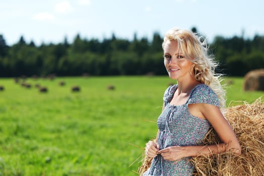 portrait of a girl next to a stack of hay under the blue sky