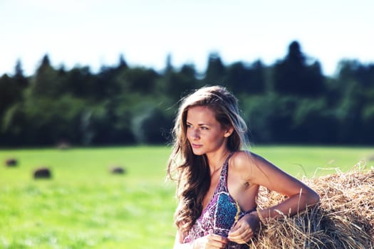 portrait of a girl next to a stack of hay under the blue sky
