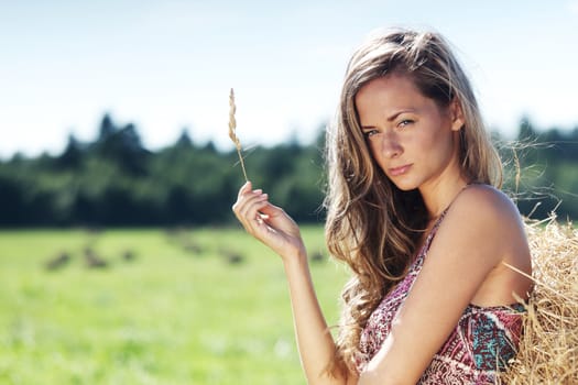 portrait of a girl next to a stack of hay under the blue sky