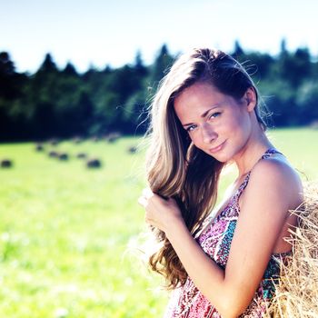 portrait of a girl next to a stack of hay under the blue sky