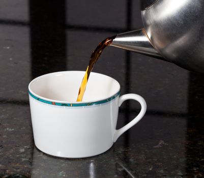 Fresh tea being poured into white cup on marble kitchen worktop