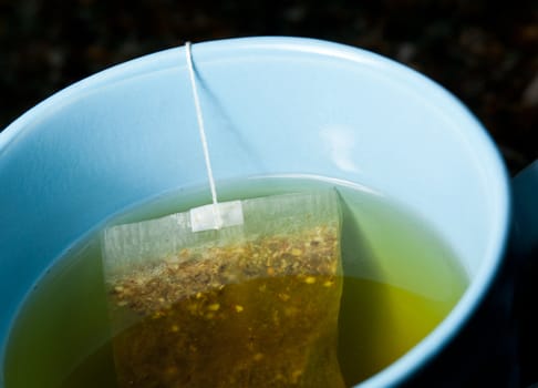 Macro of a green tea teabag brewing in hot water in a blue mug on kitchen worktop