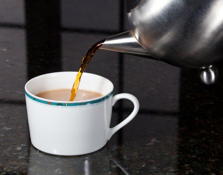 Fresh tea being poured into white cup on marble kitchen worktop