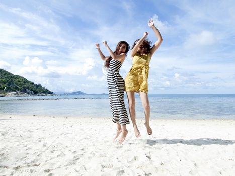 woman jumping together on sand beach with blue sky background