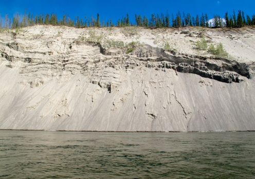 High cut bank of silt, sand and gravel slowly eroding by flowing water of mighty Yukon River, Yukon Territory, Canada