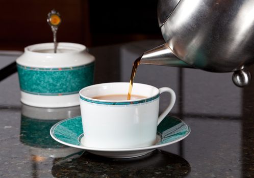Fresh tea being poured into white cup on marble kitchen worktop