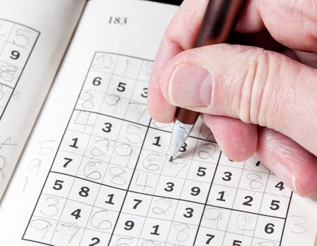 Male hand holding pen or pencil on suduko puzzle
