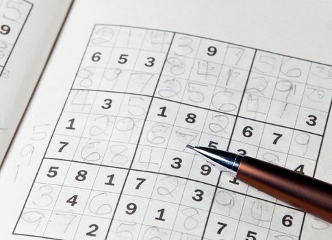 Pencil or pen resting on completed sudoku puzzle in book