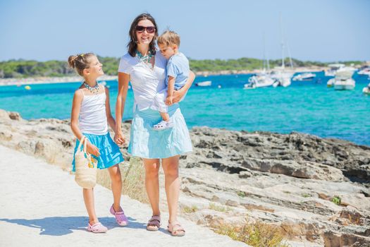 Young beautiful family of three walking along tropical beach