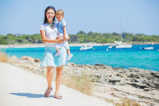 Young beautiful woman wis her son walking along tropical beach