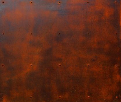 Brown and red rusted steel plate with rows of screw heads