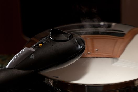 Steam escaping from lid of pressure cooker with reflection of modern kitchen