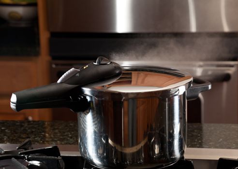 Steam escaping from lid of pressure cooker with reflection of modern kitchen
